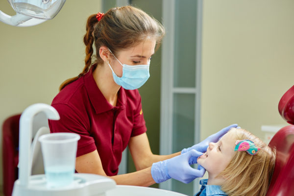 Pediatric dental assistant helping child patient